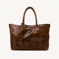 A distressed brown leather tote bag with dual top handles and a hanging leather tag with silver-tone rings, photographed against a clean white background.